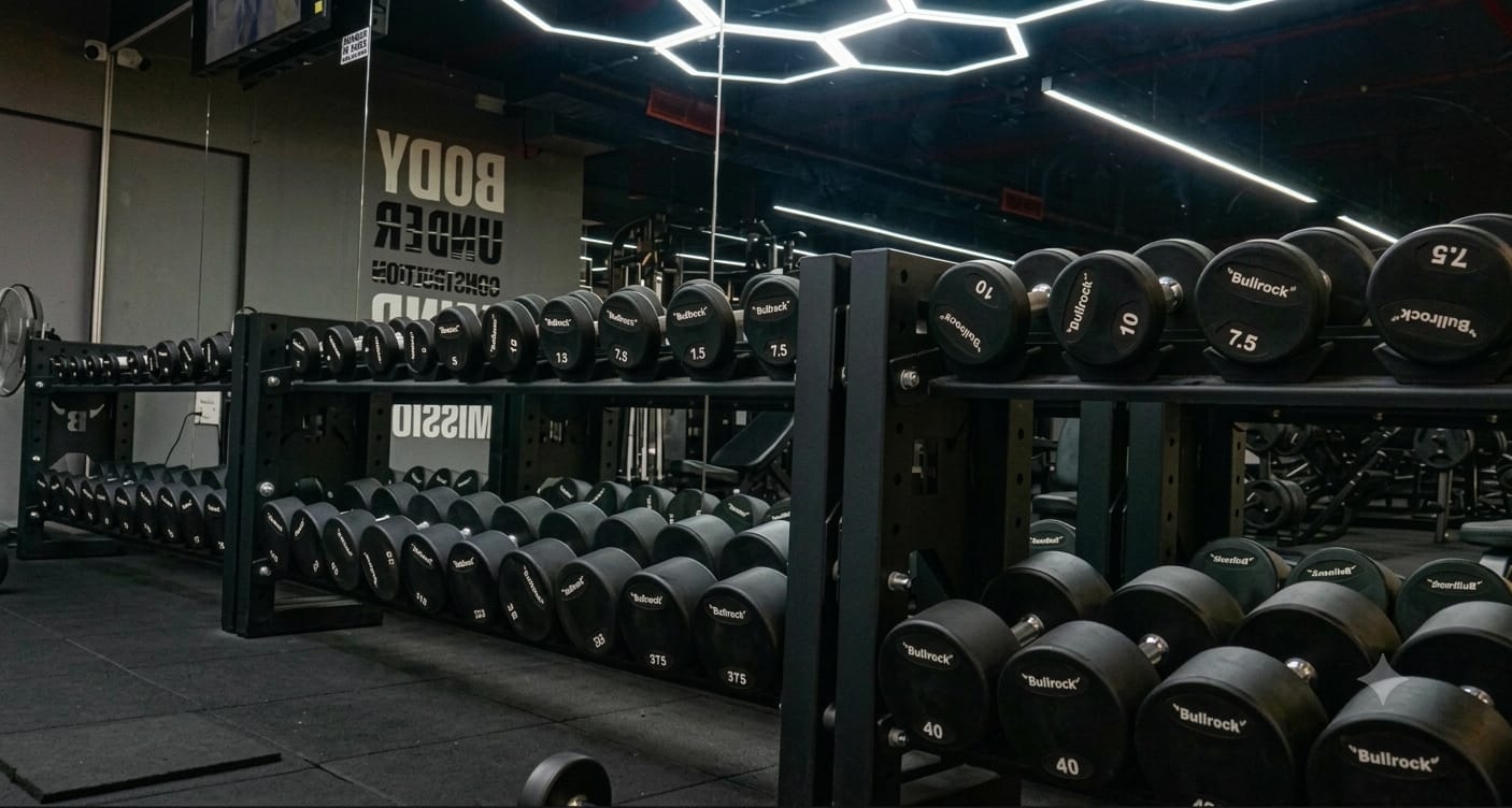 The dumbbell wall at DSigniteFitness beneath the 'Body Under Construction' mural